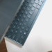 Close-up of a blue-grey ASUS laptop keyboard and lid edge on a wooden desk