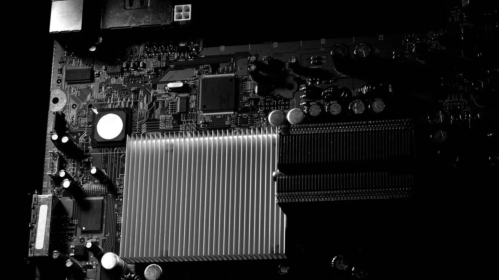 Close-up of a dark circuit board with a large finned heatsink, desaturated high-contrast photo