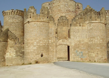 Stone medieval castle with crenellated towers and an arched gate, blue sky, graffiti on the wall