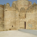 Stone medieval castle with crenellated towers and an arched gate, blue sky, graffiti on the wall