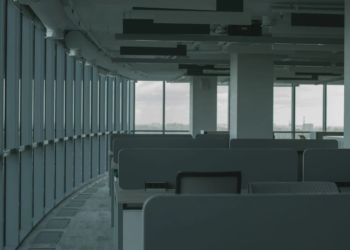 Empty modern office with rows of vacant cubicle desks beside floor-to-ceiling windows