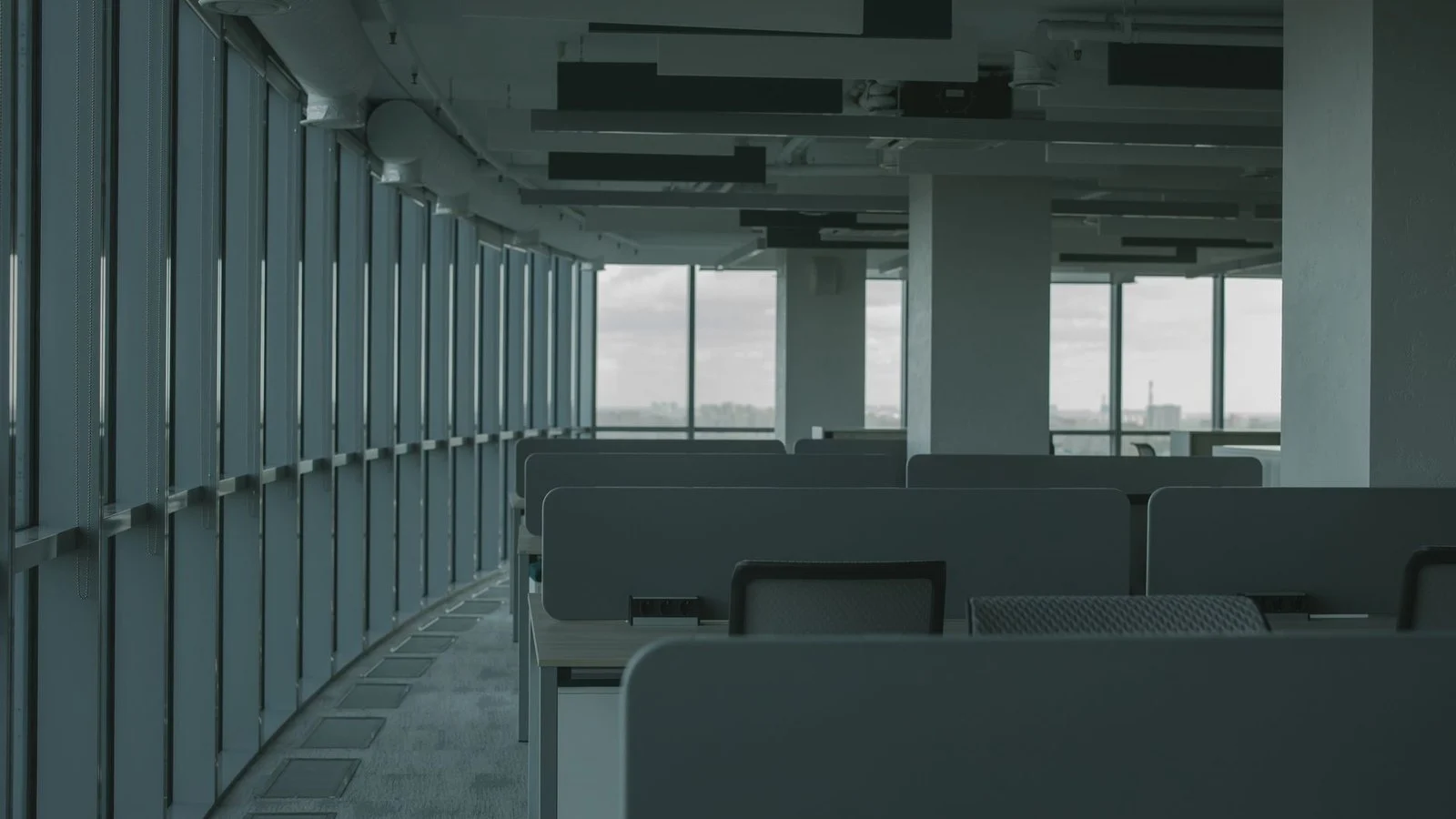 Empty modern office with rows of vacant cubicle desks beside floor-to-ceiling windows