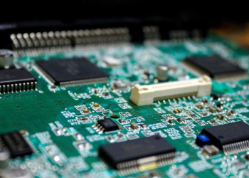 Close-up of a green circuit board with black surface-mount chips and a white connector