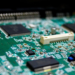 Close-up of a green circuit board with black surface-mount chips and a white connector