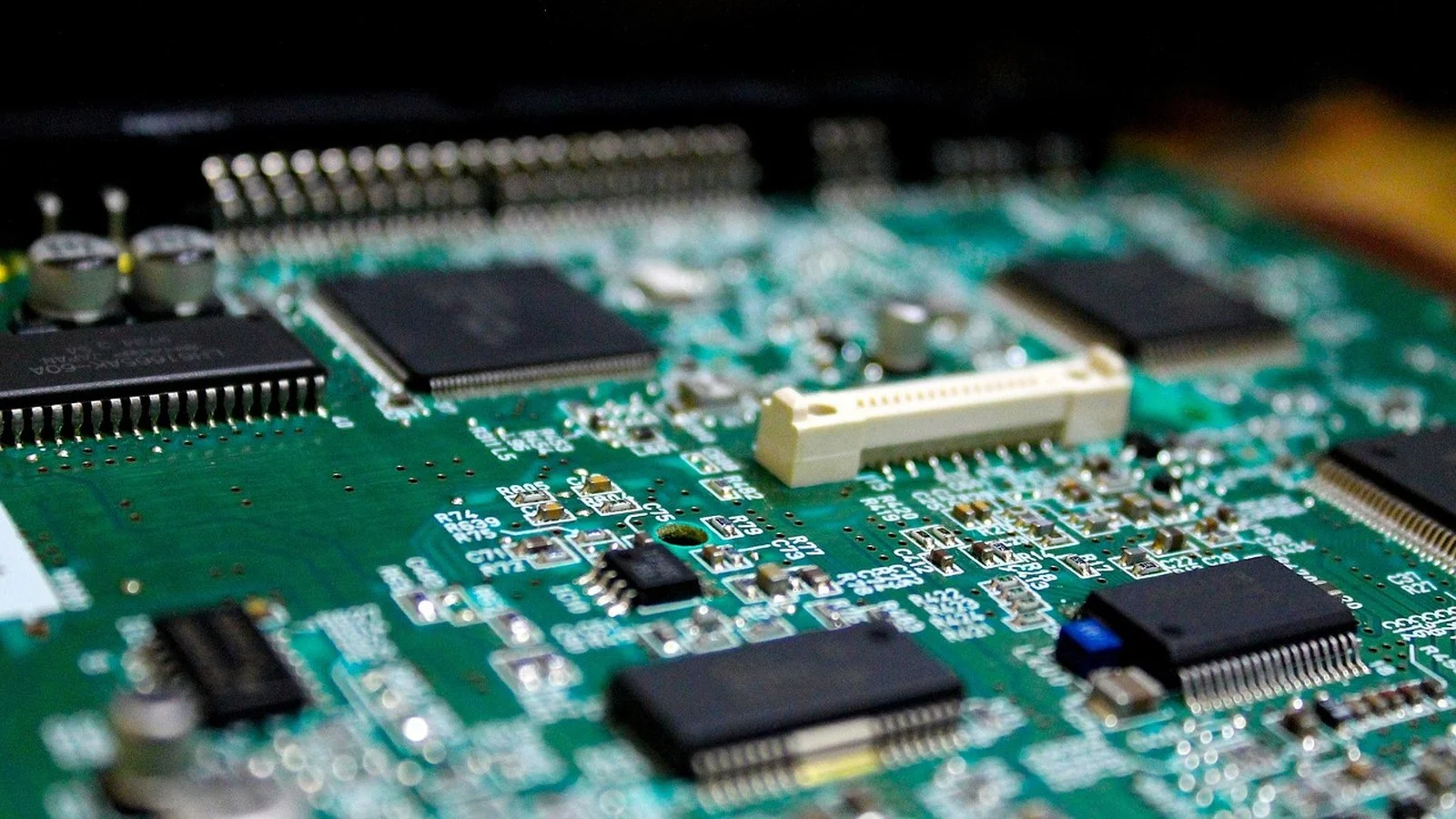 Close-up of a green circuit board with black surface-mount chips and a white connector