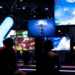 Convention attendees at gaming demo stations under screens reading 'Destiny 2 Forsaken.'