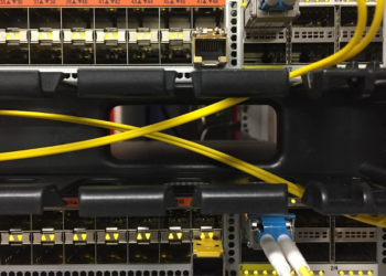 Close-up of a network switch with yellow fiber patch cables crossing between rack rails