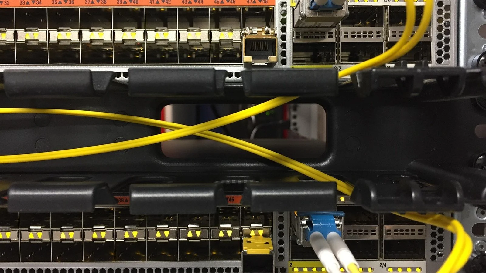 Close-up of a network switch with yellow fiber patch cables crossing between rack rails