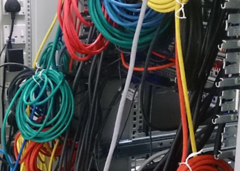 Tangled colored network patch cables running into a server rack panel