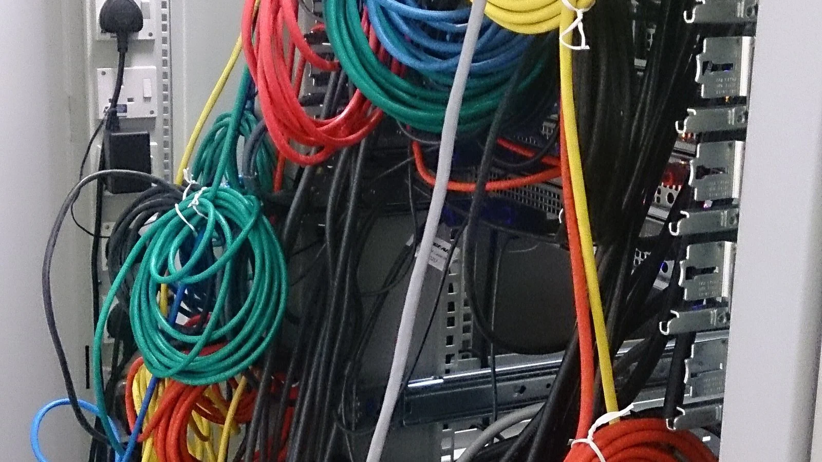 Tangled colored network patch cables running into a server rack panel