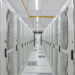 Server room aisle with rows of perforated white equipment cabinets and raised floor vents