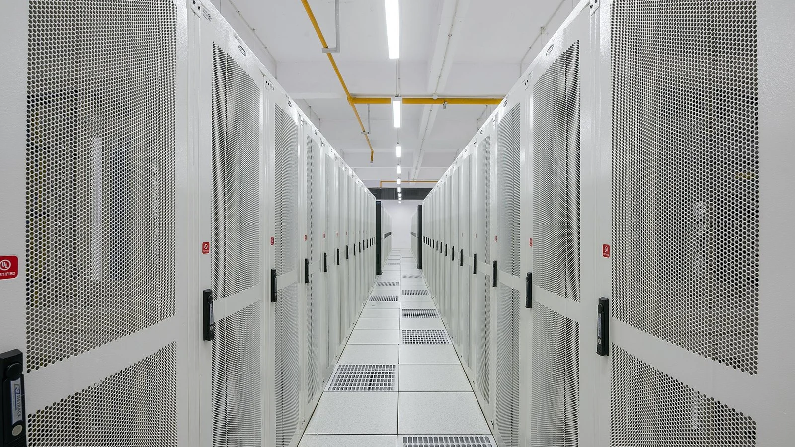 Server room aisle with rows of perforated white equipment cabinets and raised floor vents