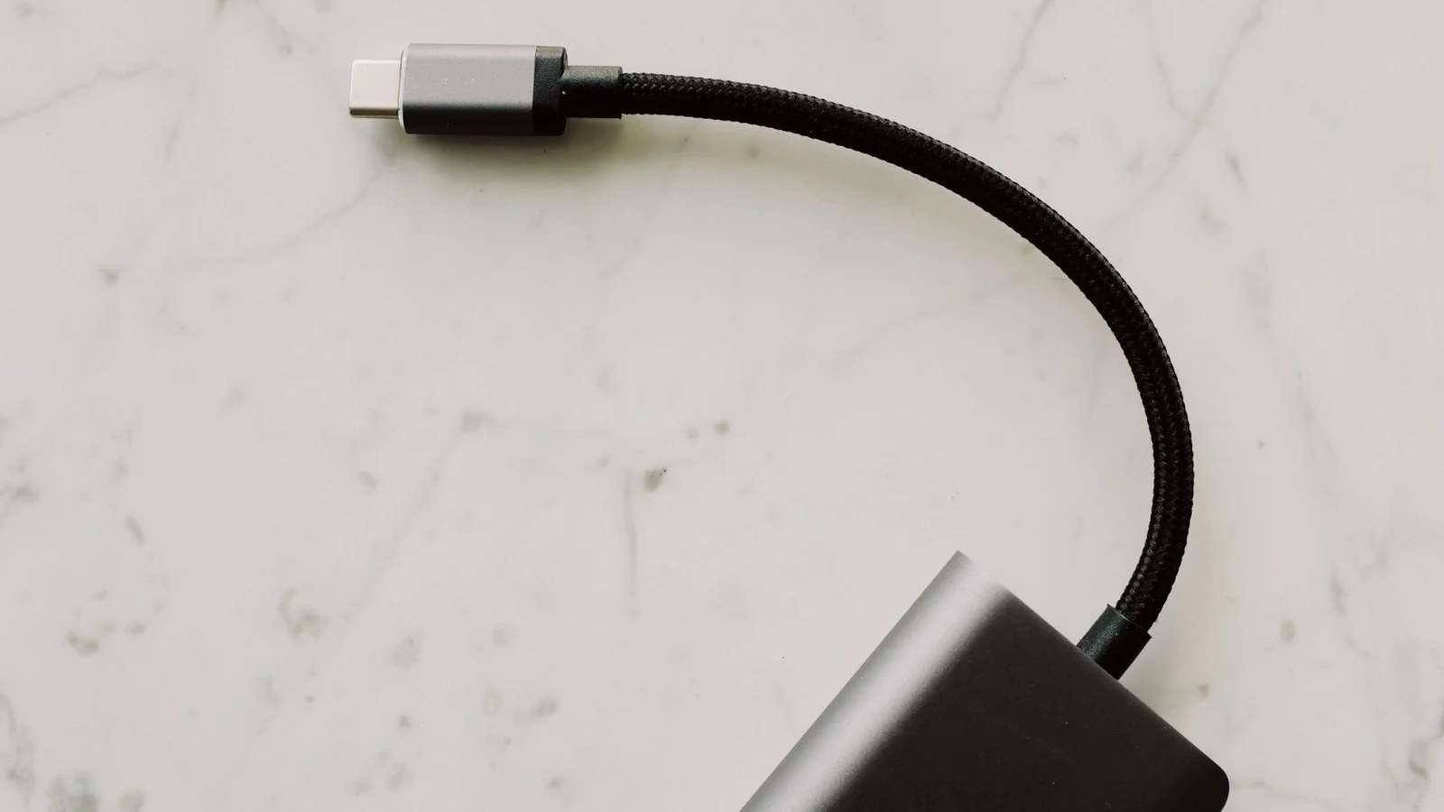 Braided USB-C cable plugged into a small black device on a marble surface