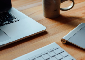 MacBook, wireless keyboard, trackpad, and a ceramic mug on a wooden desk