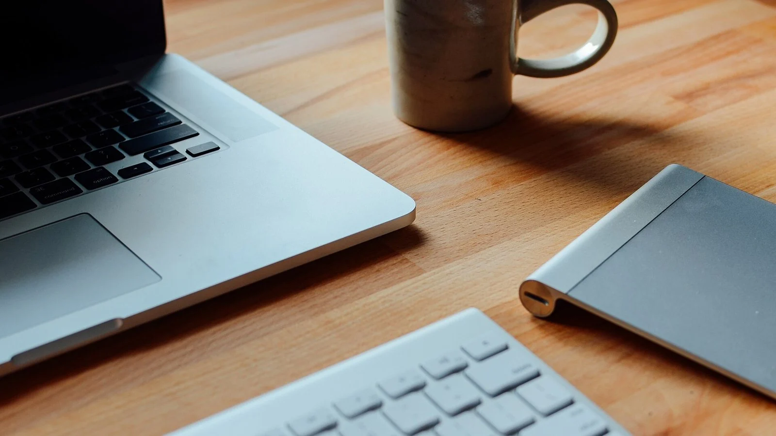 MacBook, wireless keyboard, trackpad, and a ceramic mug on a wooden desk