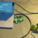 Laptop showing terminal text beside a floppy disk, floppy drive, and CDs, with cables on a concrete floor