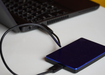 A blue and black portable external hard drive connected by USB cable to a laptop on a white desk