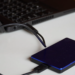 A blue and black portable external hard drive connected by USB cable to a laptop on a white desk