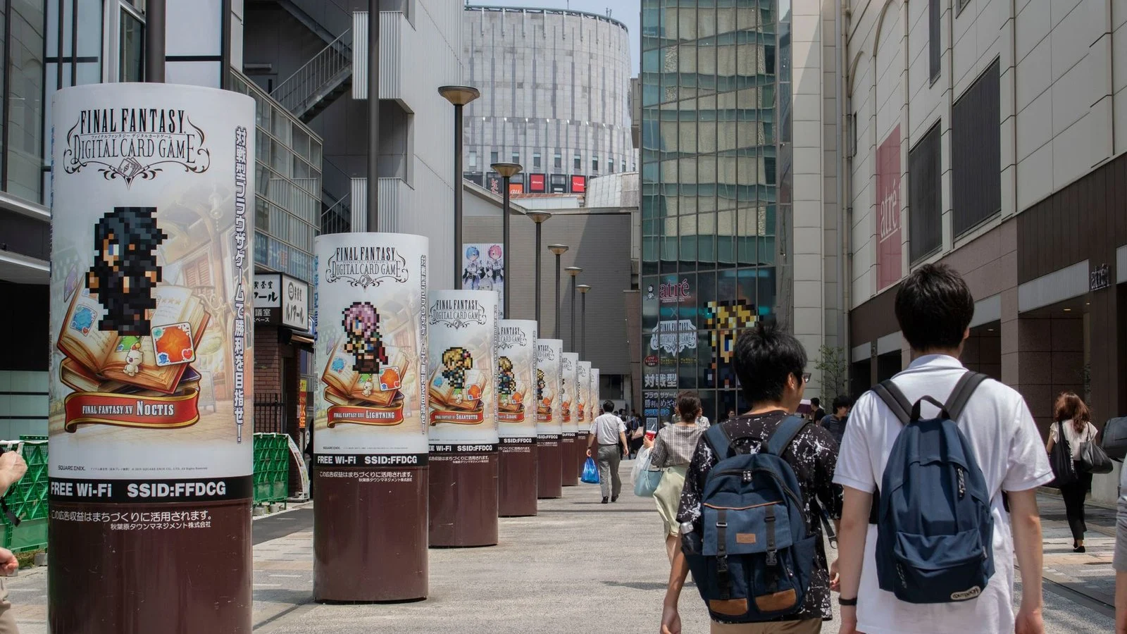 Street-side cylindrical pillars advertising Final Fantasy Digital Card Game in a Japanese shopping district