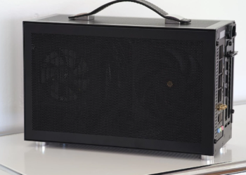 Black mesh-paneled mini-PC with leather carry handle on a white table, side panel closed