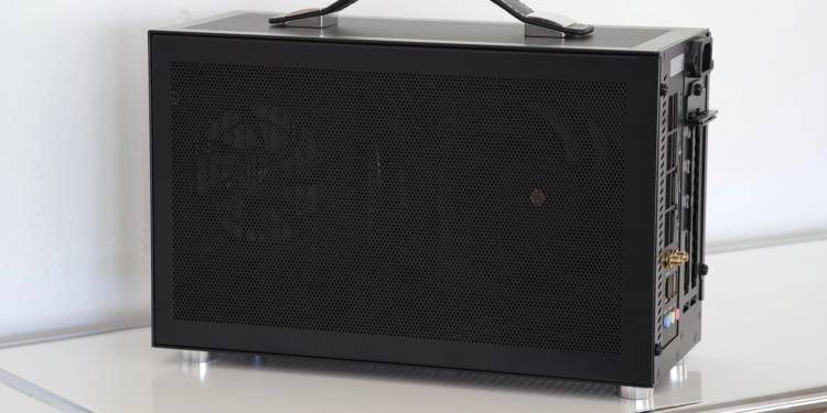 Black mesh-paneled mini-PC with leather carry handle on a white table, side panel closed