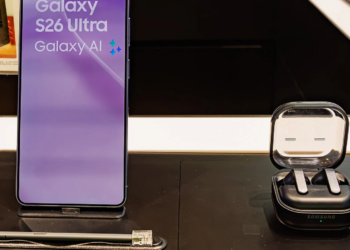 Samsung Galaxy S26 Ultra on a store display stand beside a Samsung earbuds case, purple lock screen lit