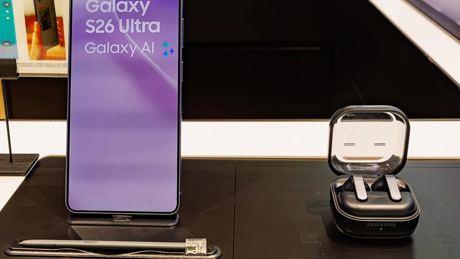 Samsung Galaxy S26 Ultra on a store display stand beside a Samsung earbuds case, purple lock screen lit