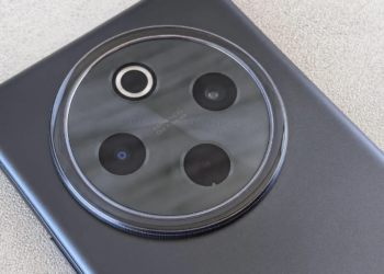 Macro shot of a phone's dark gray circular rear camera module with four lenses on a textured table