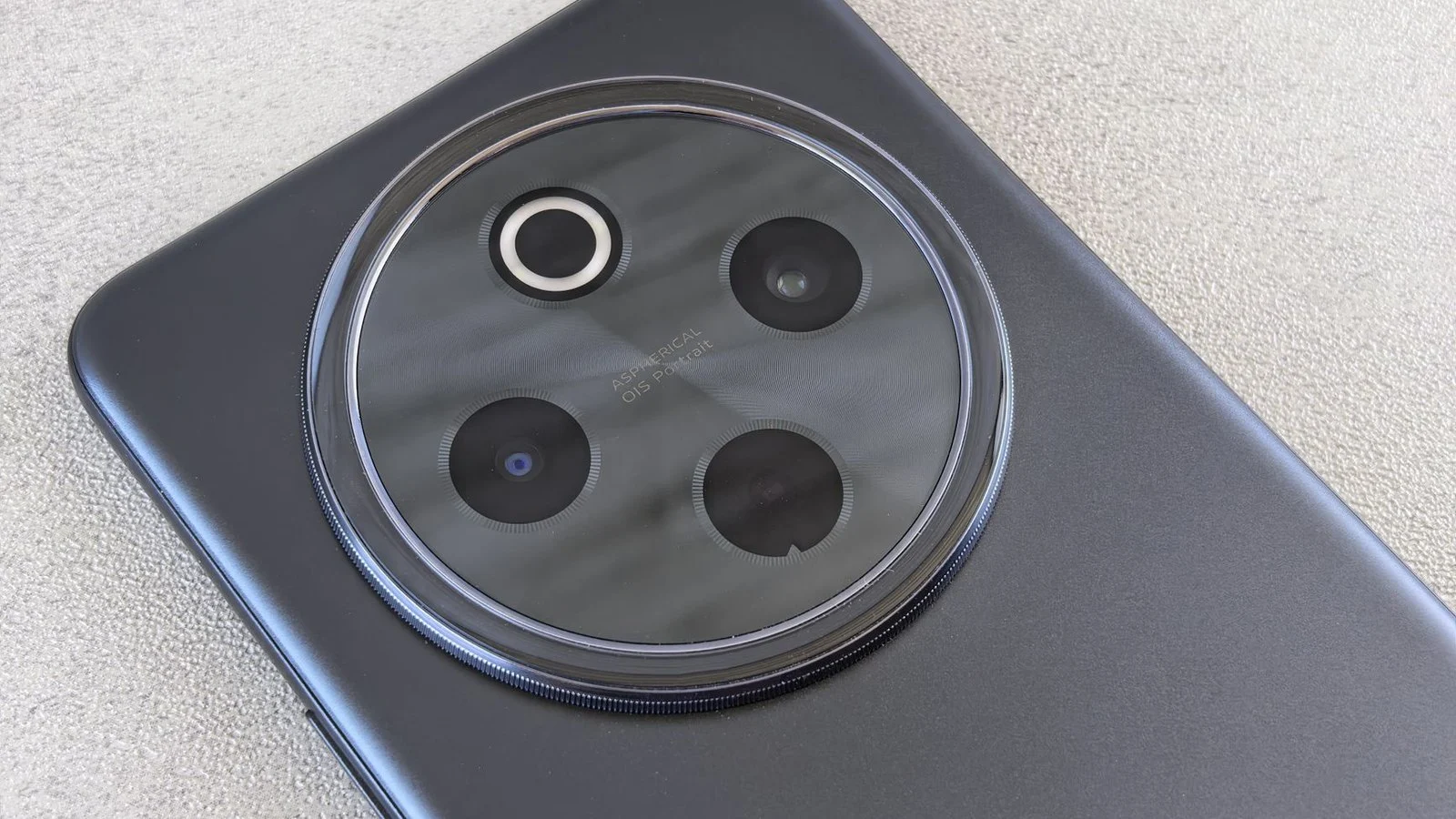 Macro shot of a phone's dark gray circular rear camera module with four lenses on a textured table