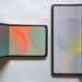 Two rose-gold foldable phones lying half-open on a white desk showing colorful wallpaper