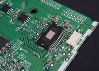 Close-up of a leaded black chip soldered on a green circuit board with test points
