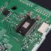 Close-up of a leaded black chip soldered on a green circuit board with test points