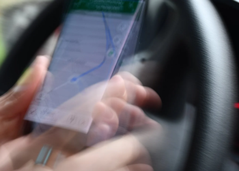 Blurred photo of a hand holding a phone showing a map route while driving a car
