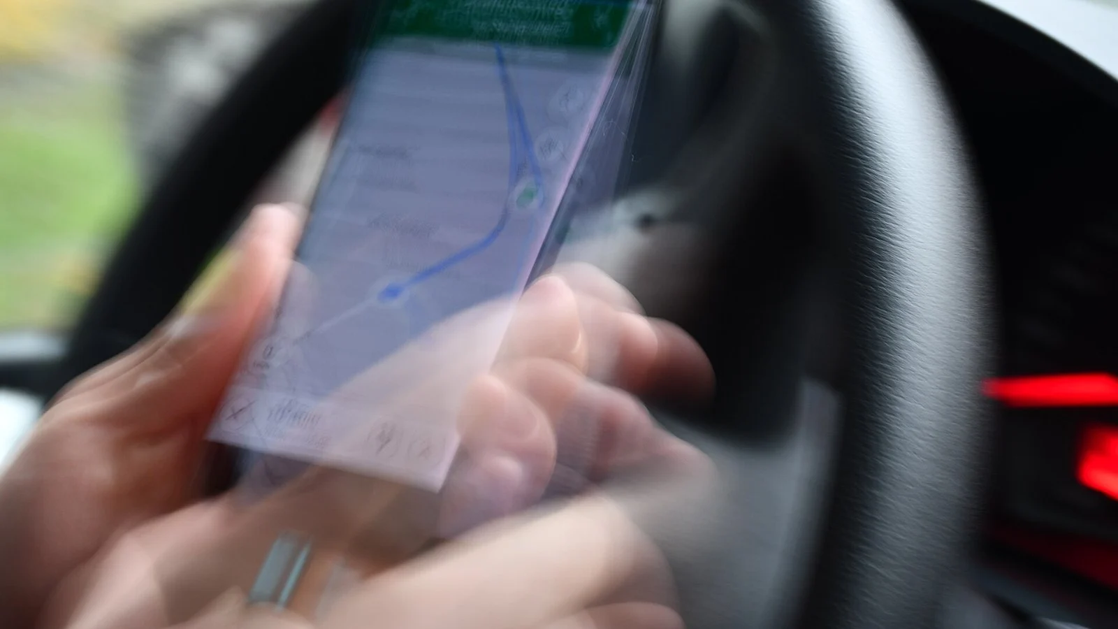 Blurred photo of a hand holding a phone showing a map route while driving a car