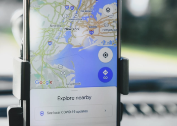 Smartphone in a car dashboard mount showing Google Maps overview of New York with an Explore Nearby panel