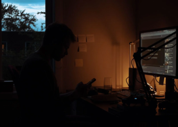 Silhouette of a person checking a phone at a desk with a glowing monitor at night