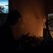 Silhouette of a person checking a phone at a desk with a glowing monitor at night