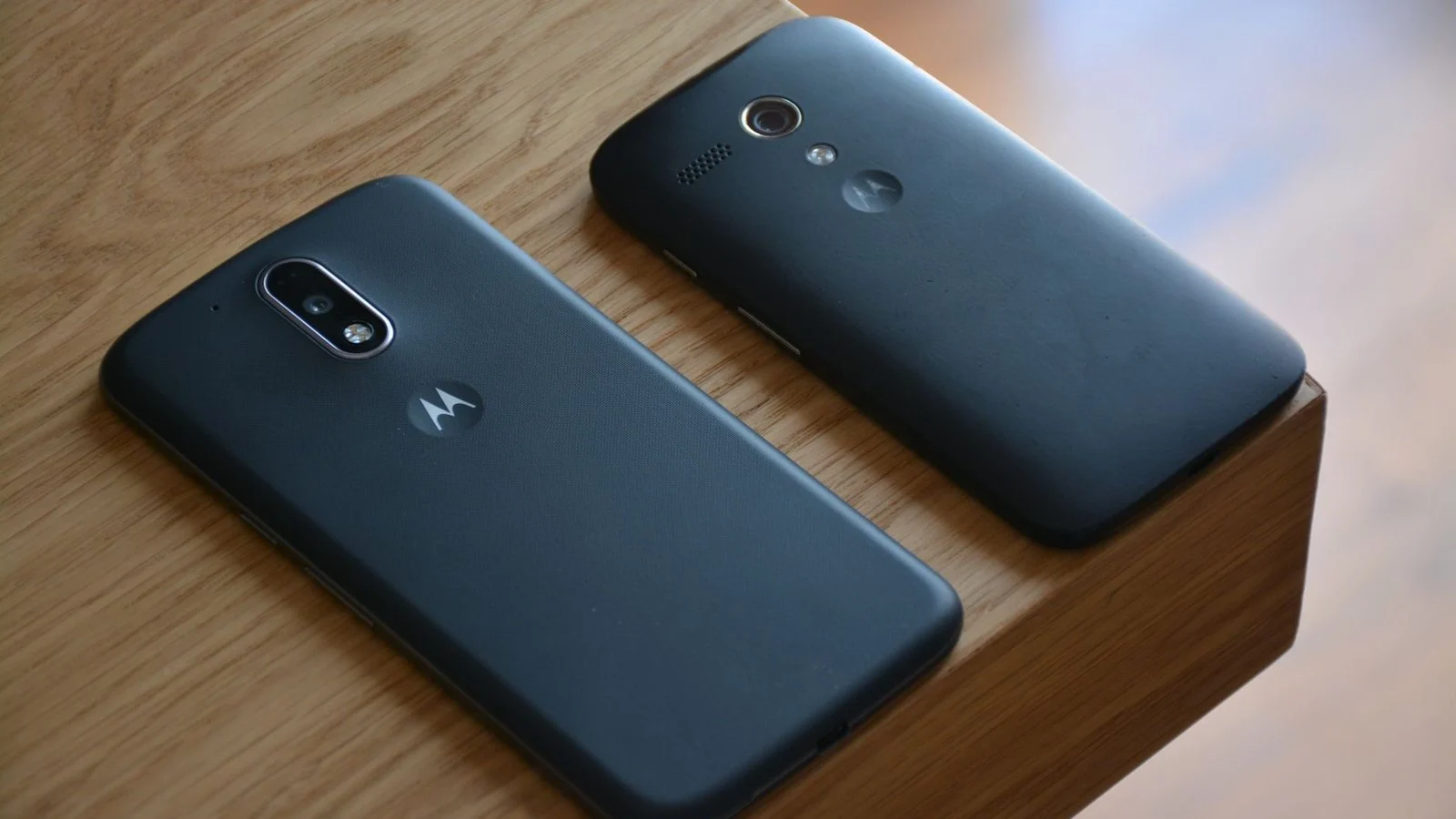 Two dark-colored older Motorola phones lying face-down on a wooden surface