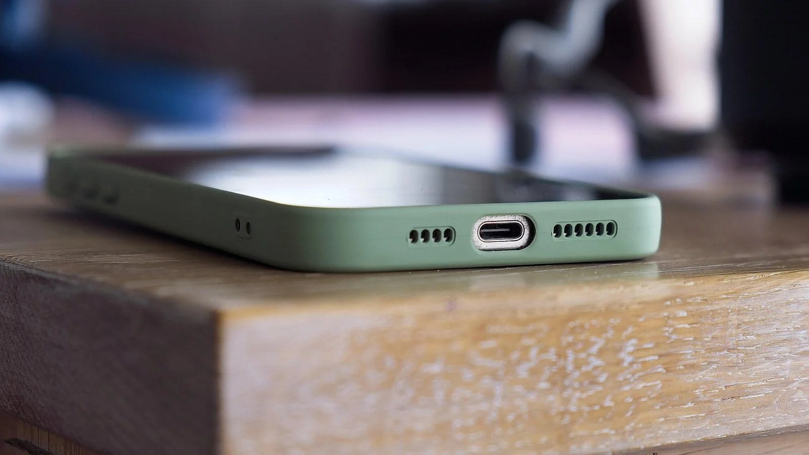 Close-up of a green-cased smartphone's USB-C port edge resting on a wooden table