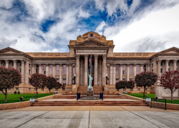 Neoclassical courthouse building with columned facade and Statue of Liberty replica on lawn