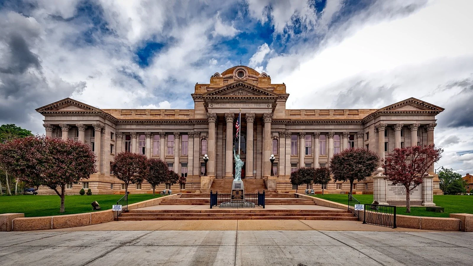 Neoclassical courthouse building with columned facade and Statue of Liberty replica on lawn