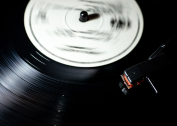 Black vinyl record spinning on a turntable with tonearm and stylus lowered, no visible branding