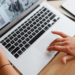 Hands on a silver laptop trackpad and keyboard, screen showing a grid of photo thumbnails