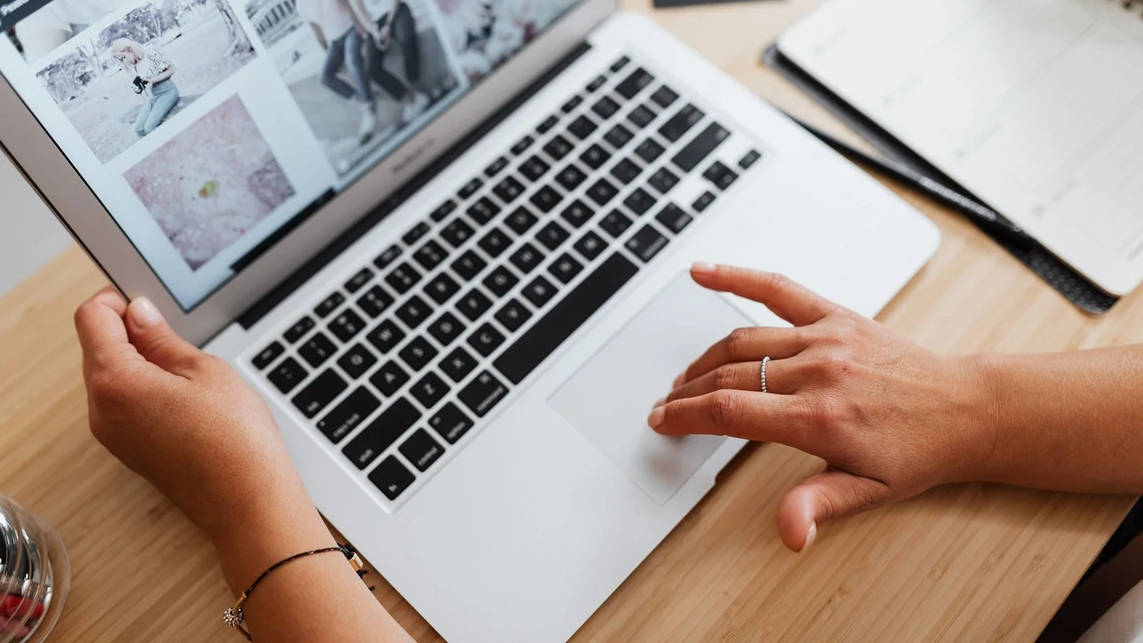 Hands on a silver laptop trackpad and keyboard, screen showing a grid of photo thumbnails