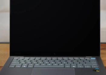 Dark gray laptop with screen off, HP logo on bottom bezel, keyboard and trackpad visible, on wood desk