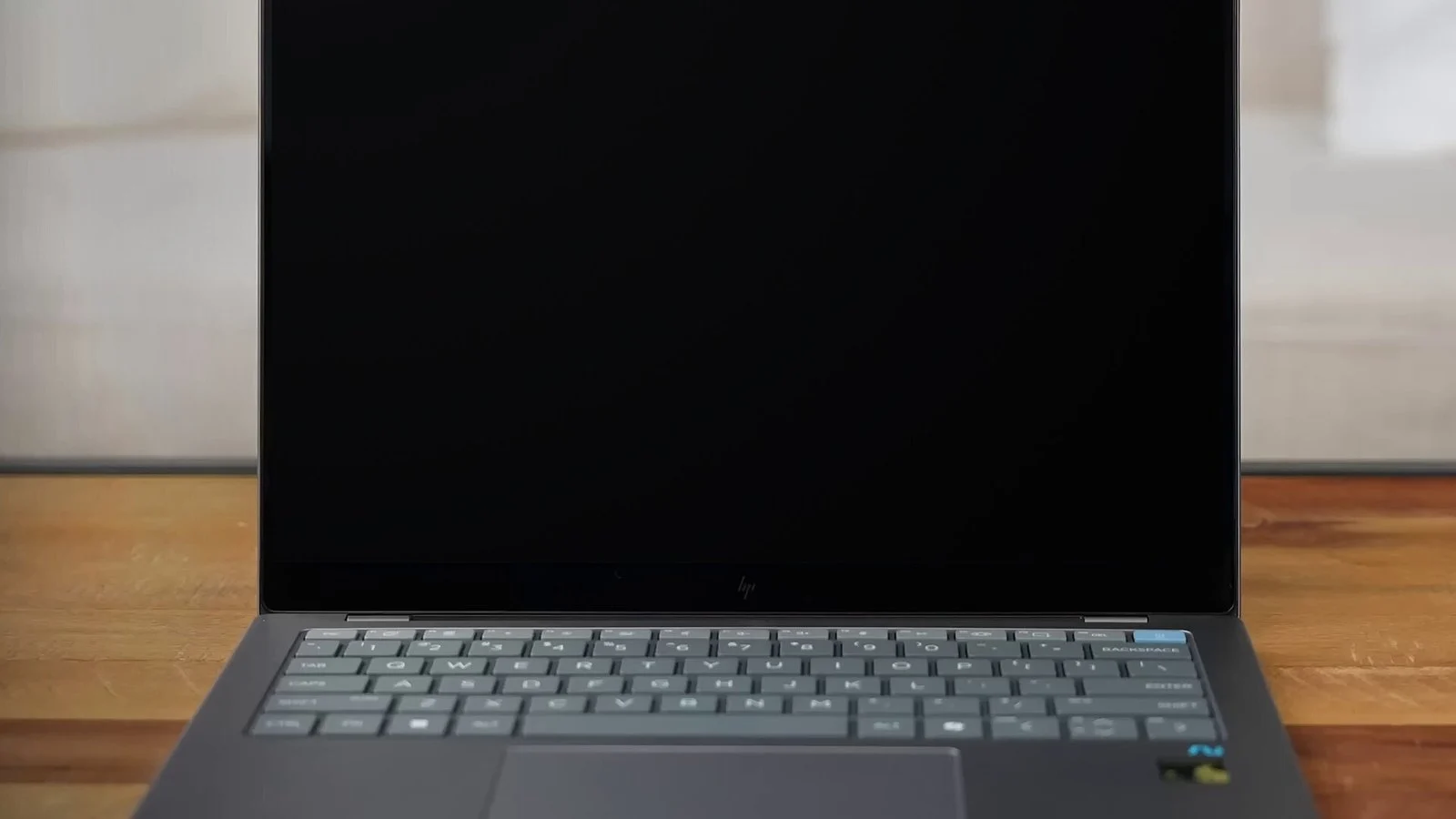 Dark gray laptop with screen off, HP logo on bottom bezel, keyboard and trackpad visible, on wood desk