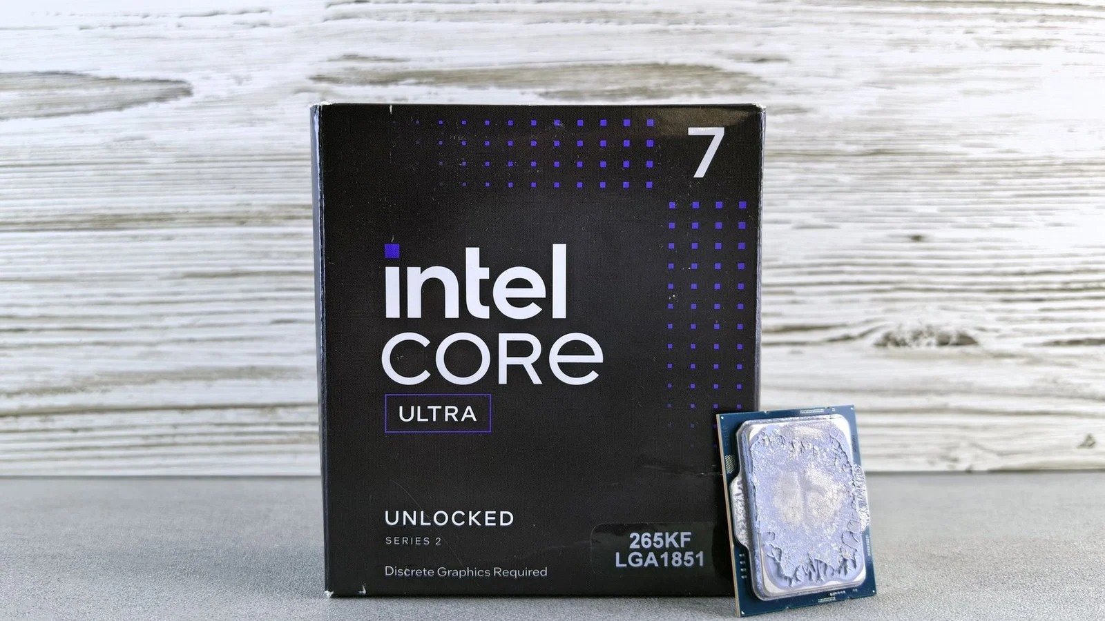 Boxed Intel Core Ultra 7 265KF processor beside its LGA1851 chip on a wood-and-concrete backdrop