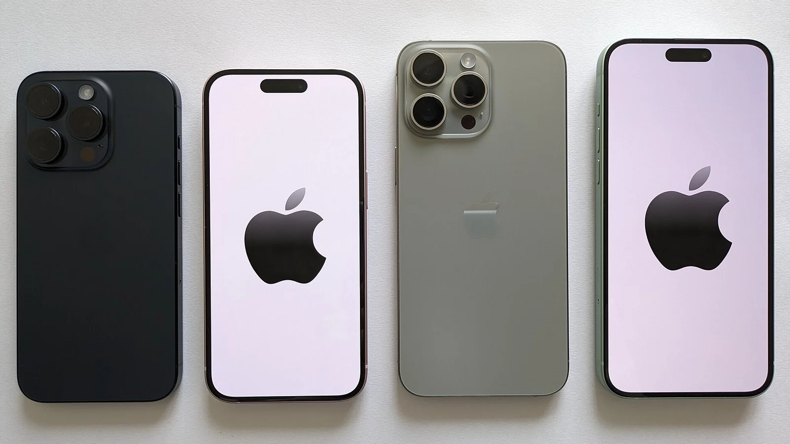 Four iPhones laid flat for comparison: dark blue, white with lavender screen, sage green, and green