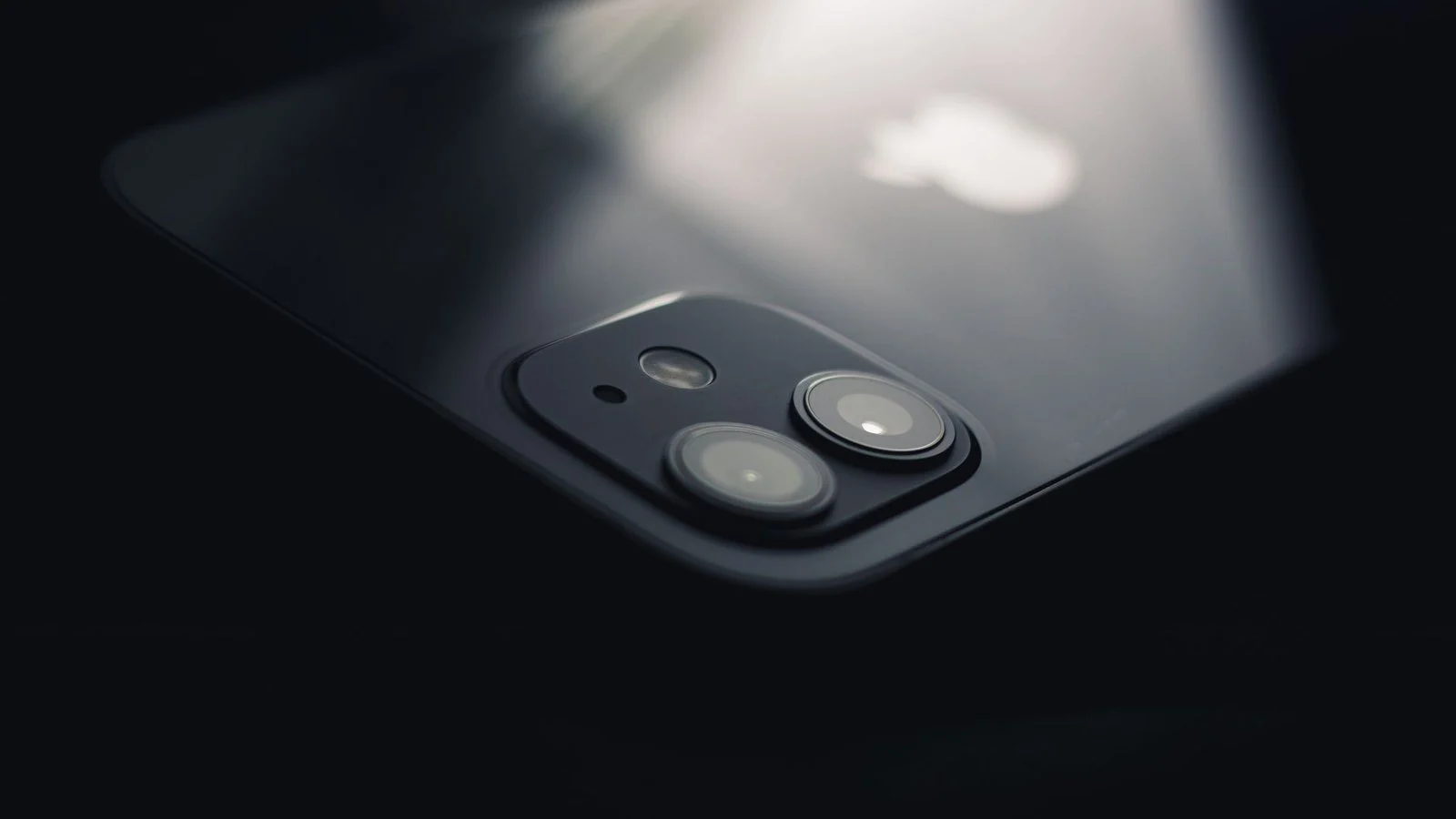 Close-up of an iPhone's glass back and dual rear camera lenses lit from above
