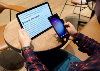Man holds a Samsung phone while reading a medical text article on a flat tablet at a cafe table